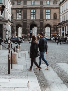 femme en manteau noir et jean bleu debout sur le trottoir pendant la journée
